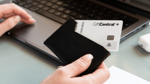 hand holding GiftCentral+ gift card while performing an online payment on a laptop